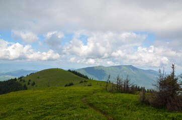 Mountain path through green grassy mountain ridge winding up in to the distant mountain peak under...