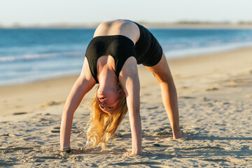 Athletic blonde woman doing the bridge position of yoga on a beach
