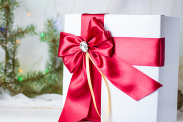 A Christmas gift decorated with a beautiful bow on a light background with a fir twig. Gifts, joy, surprise. Selective focus. the concept of Christmas and New Year