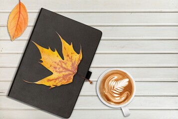 a cup of tea and a book on a wooden surface against the background of fallen leaves, autumn season