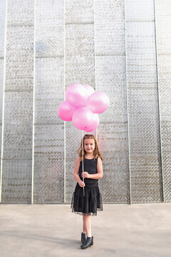 Young girl holding pink balloons in front of a metal wall.