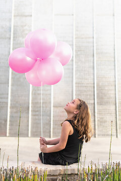 Young girl looking at pink balloons in front of a metal wall.