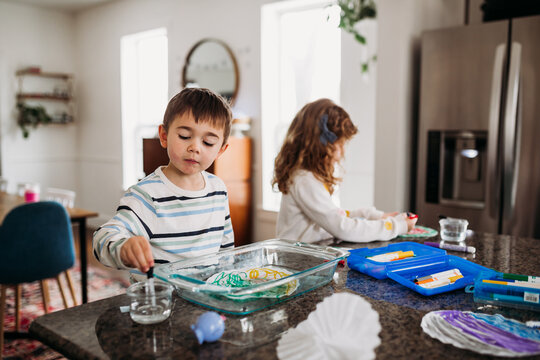 Young brother and sister doing arts and crafts at kitchen island