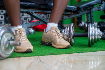 Morning workout routine in home gym. Fitness motivation and muscle training concept. Man in sneakers tying shoelaces. Athlete starting exercise with dumbbell weight.