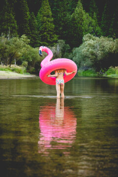 Girl wading through river and carrying flamingo floatie