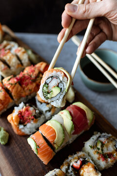 Close up of hand holding sushi roll using chopsticks above a platter.