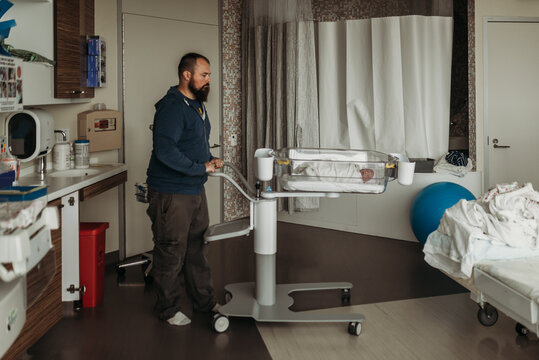 Father moving newborn baby boy's son bassinet in hospital birthing cen