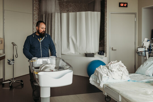 Father moving newborn baby boy's son bassinet in hospital birthing cen