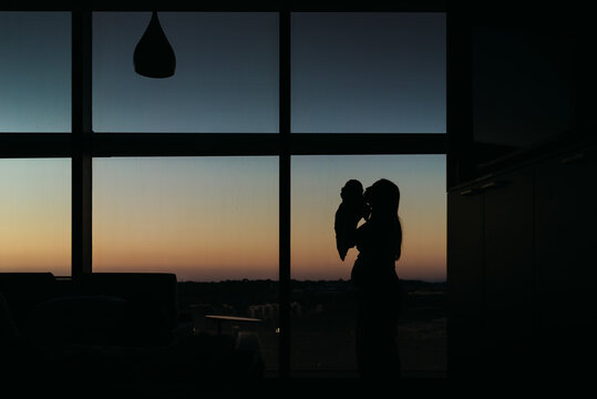 Silhouette of mother kissing newborn in hospital room at sunset
