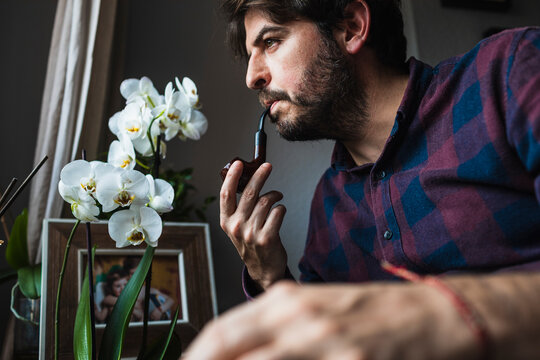 A man in his 40s looks out of a window smoking a pipe. Concept of bein