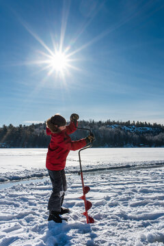Young boy using auger to make a hole in the ice on a sunny winter day.