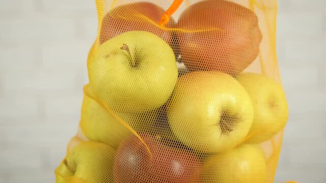 Juicy fruits in a bag. A view of a full knitted mesh with juicy apples in it on the table.