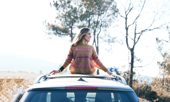 smiling pretty girl leaning out of the convertible roof of the car during a trip to the forest on vacation.