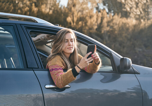 girl smiling in the car window while consulting mobile phone to talk with her friends.