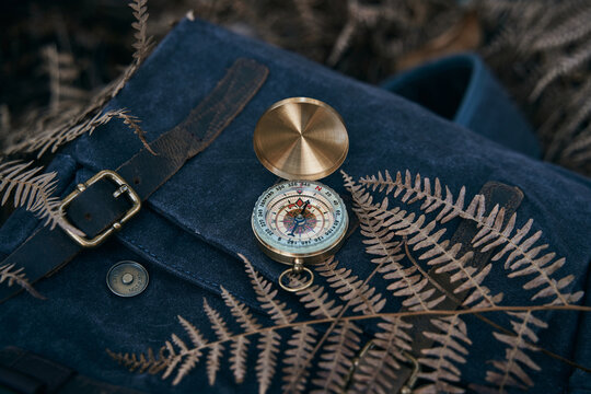 Antique gold compass on top of a backpack in nature to guide the way to the treasure.