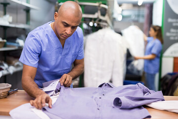 Portrait of man laundry worker checking clean clothes at dry-cleaning facility
