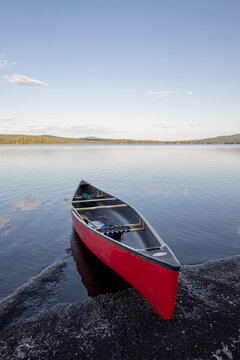 Red canoe pulled up on rocky shore of pristine calm lake in Maine