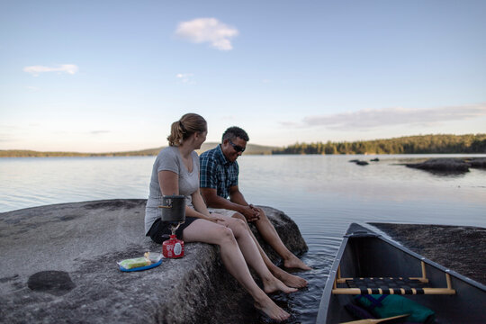 interracial couple sit on lake shore with canoe and cook dinner