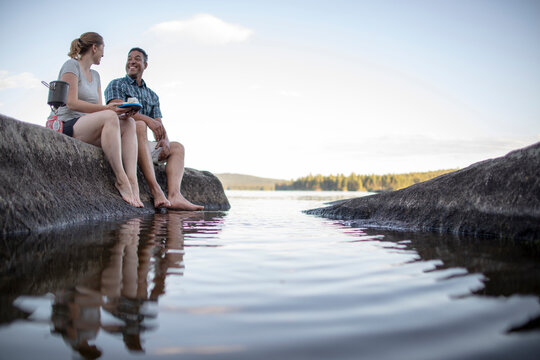 Multi racial couple sit on rock on edge of lake on pristine lake Maine