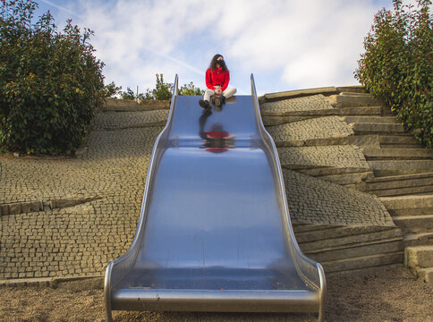 young woman sitting on top of a metal slide with mask