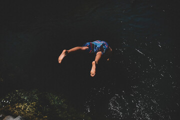 Feet Flying, as Boy in Colorful Suit Dives into Dark Water
