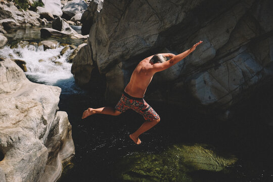 Boy in Colorful Swim Trunks Leaps from a Cliff into a Beautiful River