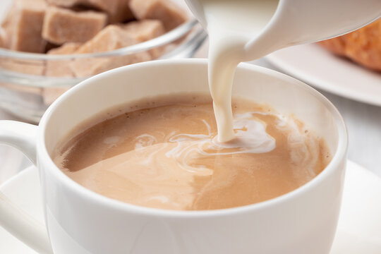 Pouring milk or cream into freshly brewed coffee, close up