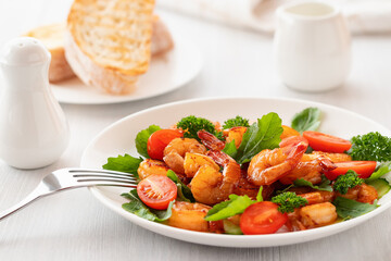Fresh salad of shrimps, tomatoes, arugula and herbs on a white plate