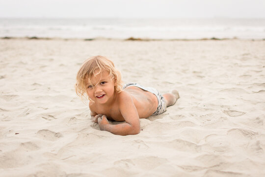 Blonde toddler boy crawling on his belly in the sand at the beach