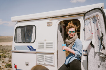 A stylish young woman drinks coffee outside of her trailer in the sun