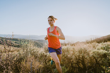 Athletic blonde woman trail runs in the mountains at golden hour