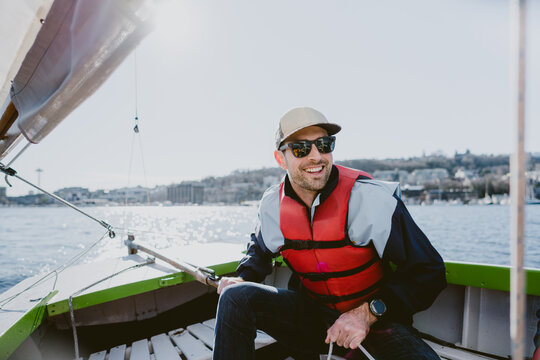 A handsome young man smiles and sails a small boat on a sunny day