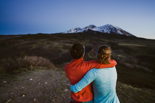 Two female friends hug and look out at mountain view at dusk