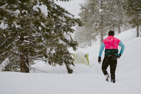A man in bright jacket walks through deep snow out his tent