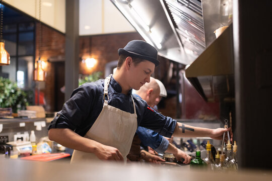 Young cook taking tongs in kitchen