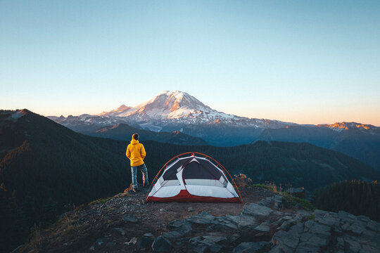 A man is standing by a tent on the top of a mountain near mt. Rainier