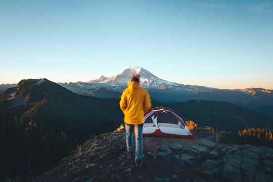 A man is walking to a tent on the top of a mountain near mt. Rainier
