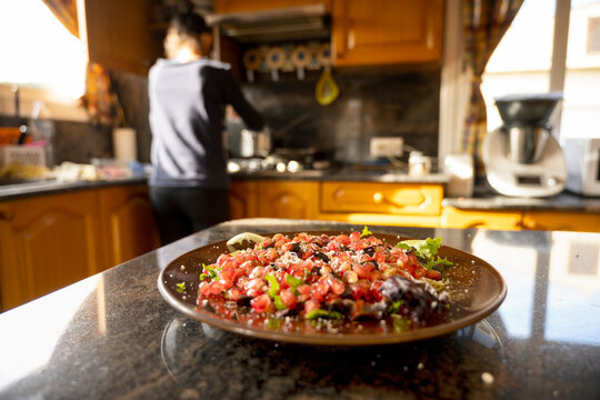 Closeup of a pomegranate salat on table while an unfocused woman cooking at kitchen