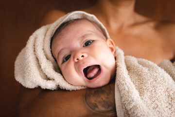 A beautiful baby rolled in a towel opening the mouth with her mother