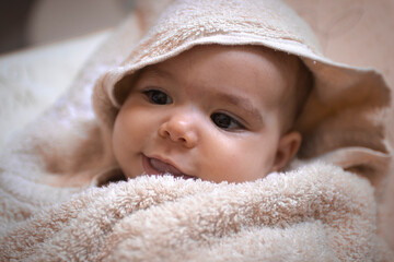A baby rolled in the towel looking around and smiling in the bath