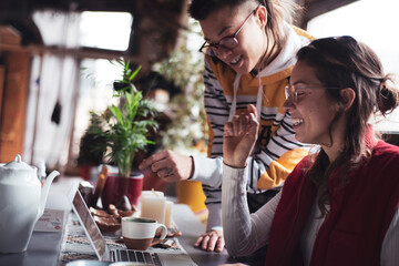 two queer business women laugh and work together on laptop at home