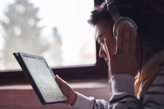fun asian person with headphone by window reads spreadsheet on screen