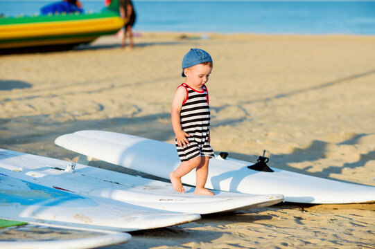 Cute little kid on a beach walking barefoot along windsurfing board