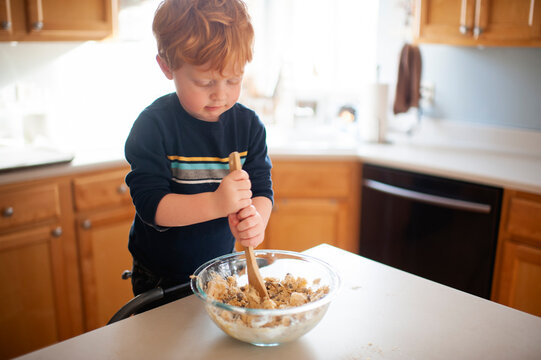 Boy 3-4 years old mixing up cookie dough at kitchen counter at home