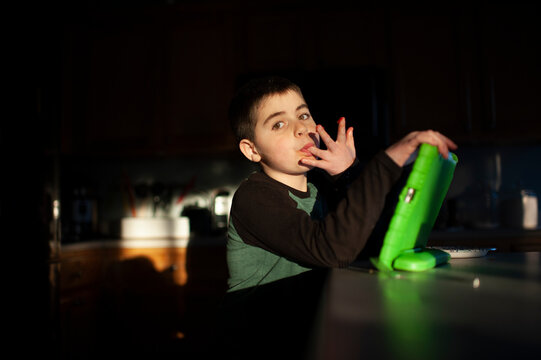 Boy 9-10 years old licks fingers while holding tablet in pretty light