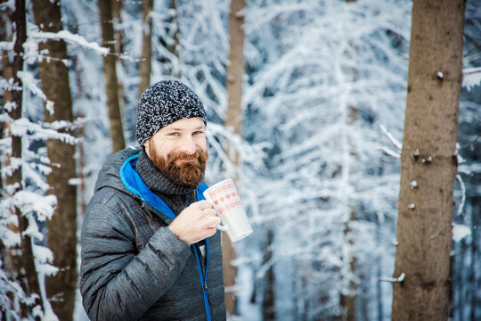 man drinking hot tea in winter forest