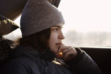 A girl in gray clothes looks out the car window, leans on her hand.