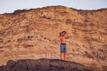 Boy standing on top of a big rock with ocean cliffs behind him.