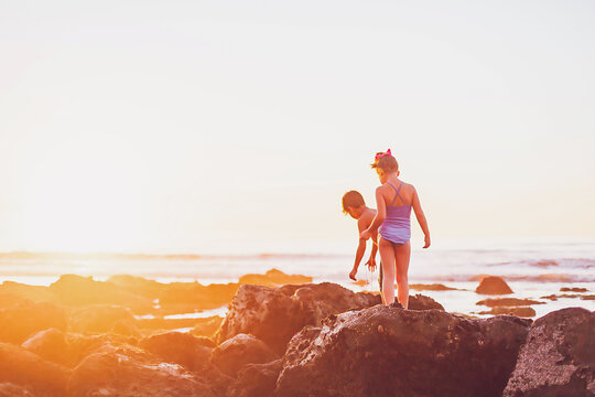 Boy and girl walking on the rocks at the beach at low tide at sunset.