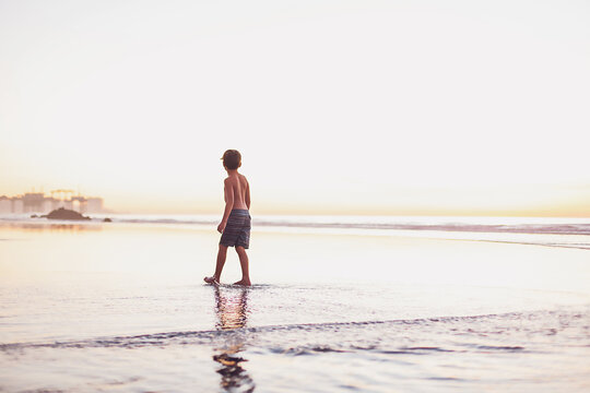 Boy walking at low tide at the beach during sunset hours.